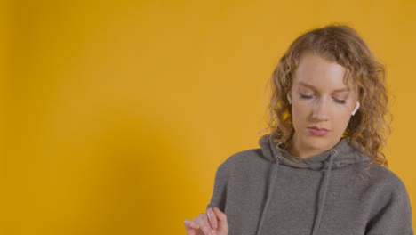 Studio-Shot-Of-Young-Woman-Listening-To-Music-On-Mobile-Phone-And-Dancing-Against-Yellow-Background