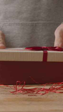 Vertikales-Video-Eines-Mannes,-Der-Romantische,-In-Geschenkverpackung-Verpackte-Valentinsgrüße-In-Einer-Schachtel-Auf-Dem-Tisch-Abdeckt