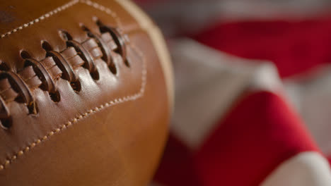 Close-Up-Shot-Of-Person-Picking-Up-American-Football-With-Stars-And-Stripes-Flag-In-Background-1