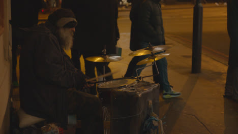 Ejecutante-De-La-Calle-O-Persona-Sin-Hogar-Tocando-La-Batería-En-La-Zona-Del-Puente-De-Londres-Reino-Unido-Por-La-Noche