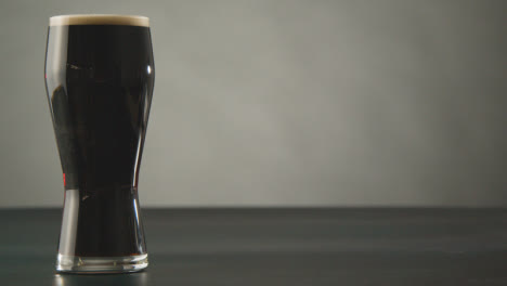 Pint-Of-Irish-Stout-In-Glass-Against-Studio-Background-To-Celebrate-St-Patricks-Day