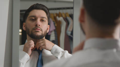 Young-Man-At-Home-Putting-On-Tie-Ready-For-Job-Interview-Reflected-In-Mirror-1