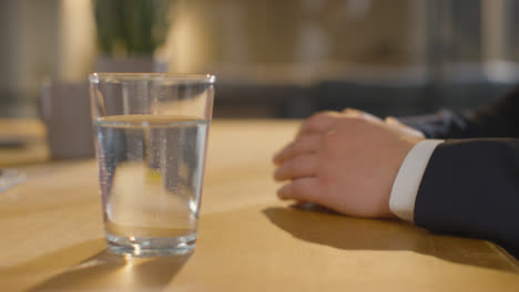 Close-Up-Showing-Hands-Of-Male-Candidate-Being-Interviewed-In-Office-For-Job-With-Glass-Of-Water