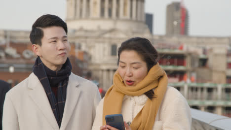 Young-Asian-Couple-On-Holiday-Walking-Across-Millennium-Bridge-With-St-Pauls-Cathedral-In-Background-2