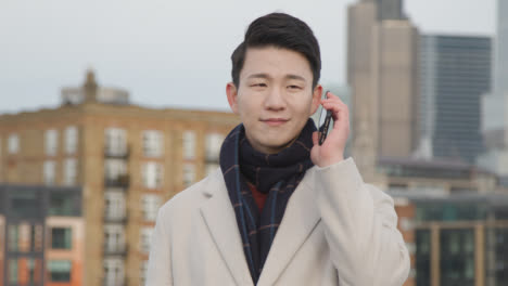Junger-Asiatischer-Geschäftsmann,-Der-Am-Handy-Mit-Der-Skyline-Der-Stadt-London-Im-Hintergrund-Spricht-2