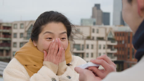 Young-Asian-Couple-With-Romantic-Man-Proposing-To-Woman-Against-City-Skyline-4