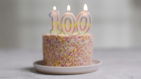 Studio-Shot-Birthday-Cake-Covered-With-Decorations-And-Candle-Celebrating-One-Hundredth-Birthday-Being-Blown-Out