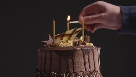 Close-Up-Studio-Shot-Of-Decorated-Chocolate-Birthday-Celebration-Cake-With-Candles-Being-Lit-Against-Black-Background-1
