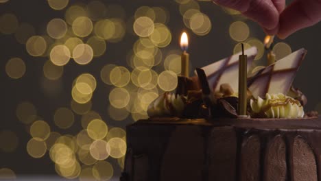 Studioaufnahme-Eines-Dekorierten-Schokoladen-Geburtstagskuchens-Mit-Kerzen,-Die-Vor-Bokeh-Hintergrundbeleuchtung-Angezündet-Werden-1