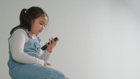 Studio-Shot-Of-Young-Girl-On-ASD-Spectrum-Gaming-On-Mobile-Phone-Against-White-Background