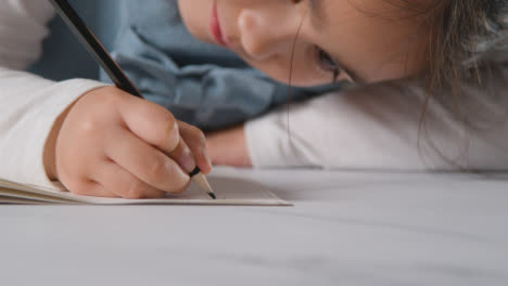 Studio-Shot-Of-Young-Girl-At-Table-Writing-In-School-Book-2