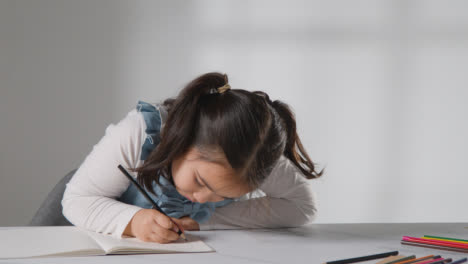 Studio-Shot-Of-Young-Girl-At-Table-Concentrating-On-Writing-In-School-Book-2