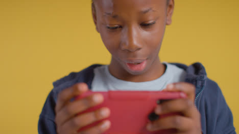 Close-Up-Of-Excited-Boy-On-ASD-Spectrum-Gaming-On-Mobile-Phone-On-Yellow-Background-