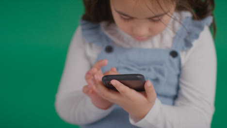 Studio-Portrait-Of-Young-Girl-On-ASD-Spectrum-Playing-With-Mobile-Phone-On-Green-Background-1