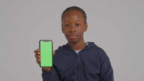 Studio-Portrait-Of-Boy-Holding-Green-Screen-Mobile-Phone-Against-Grey-Background