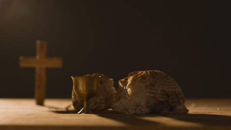 Religious-Concept-Shot-With-Chalice-Broken-Bread-Cross-And-Wine-On-Wooden-Table-Against-Black-Background-2