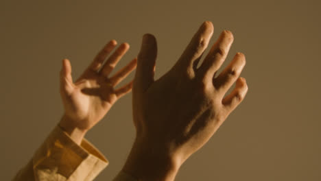 Studio-Close-Up-Shot-Of-Man-Wearing-Robes-Raising-Hands-In-Prayer
