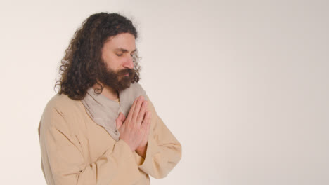 Portrait-Of-Man-Wearing-Robes-With-Long-Hair-And-Beard-Representing-Figure-Of-Jesus-Christ-Putting-Hands-Together-In-Prayer-