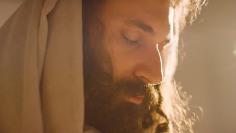 Backlit-Close-Up-Of-Man-Wearing-Robes-With-Long-Hair-And-Beard-Representing-Figure-Of-Jesus-Christ-Praying