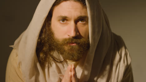 Man-Wearing-Robes-With-Long-Hair-And-Beard-Representing-Figure-Of-Jesus-Christ-Looking-Up-Into-Camera-And-Praying