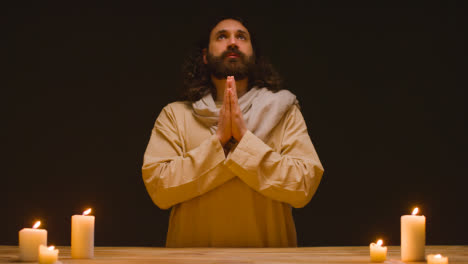 Studio-Shot-Of-Man-Wearing-Robes-Representing-Figure-Of-Jesus-Christ-Praying-At-Altar