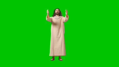 Studioaufnahme-Eines-Mannes-In-Roben-Und-Sandalen-Mit-Langen-Haaren-Und-Bart,-Der-Die-Figur-Von-Jesus-Christus-Darstellt,-Der-Die-Arme-Auf-Grünem-Bildschirm-Hebt