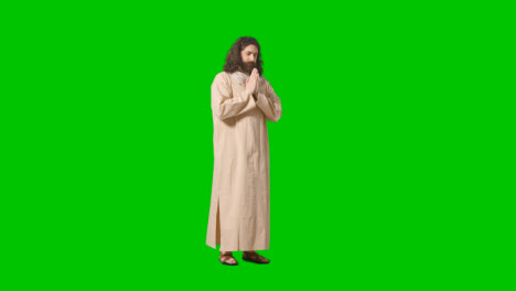 Studio-Shot-Of-Man-Wearing-Robes-And-Sandals-With-Long-Hair-And-Beard-Representing-Figure-Of-Jesus-Christ-Praying-On-Green-Screen-1
