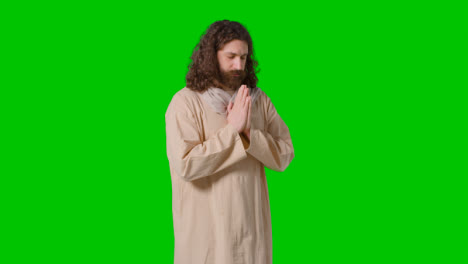 Studio-Shot-Of-Man-Wearing-Robes-With-Long-Hair-And-Beard-Representing-Figure-Of-Jesus-Christ-Praying-On-Green-Screen-1