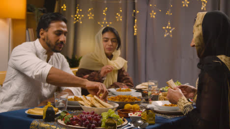 Familia-Musulmana-Sentada-Alrededor-De-La-Mesa-En-Casa-Comiendo-Comida-Para-Celebrar-Eid