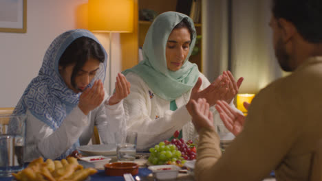 Muslim-Muslim-Family-Sitting-Around-Table-At-Home-Saying-Prayer-Before-Meal