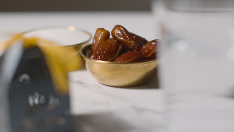 Bowl-Of-Dates-With-Glass-Of-Water-And-Gift-Boxes-On-Marble-Background-Celebrating-Festival-Of-Eid