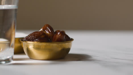 Close-Up-Of-Bowl-Of-Dates-With-Sugar-And-Glass-Of-Water-On-Marble-Surface-Celebrating-Muslim-Festival-Of-Eid