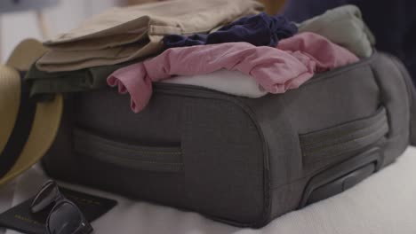 Close-Up-Of-Person-Packing-Clothes-Into-Suitcase-Ready-For-Summer-Holiday-