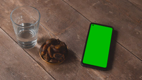 High-Angle-Shot-of-Lantern-Water-and-Dates-with-a-Green-Screen-Phone