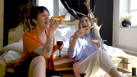 Dos-Chicas-Felices-Bebiendo-Vino-Y-Compartiendo-Pizza-Mientras-Se-Sientan-En-El-Suelo-En-Casa