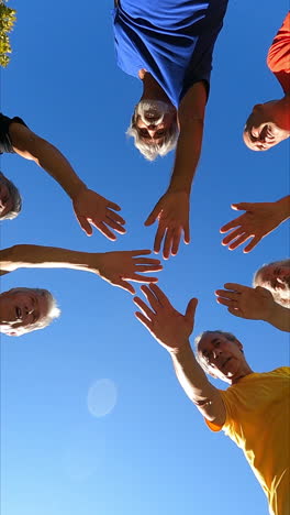 View-from-below-of-a-senior-football-team-standing-in-circle,-putting-hands-together-and-raising-up