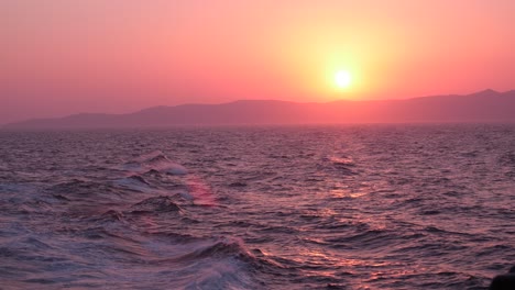 Hermosa-Puesta-De-Sol-Rosa-Sobre-El-Mar-Mediterráneo-Mientras-Las-Olas-Chocan-Con-Las-Montañas-En-El-Fondo