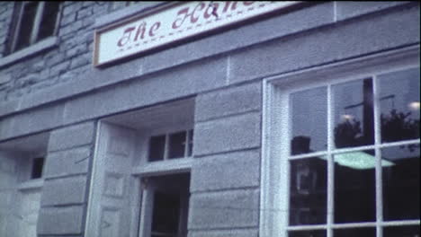 Camera-tilts-from-sign-to-limestone-building-storefront-with-pedestrians-passing-by