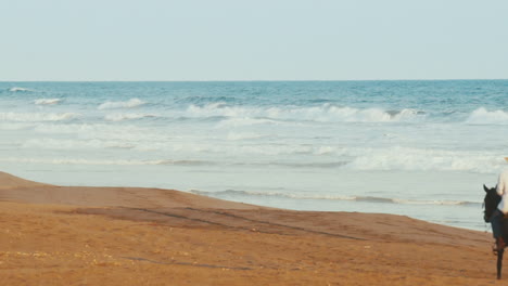 Hispanic-man-with-straw-hat-riding-horse-on-Guatemala-beach,-SLOW-MOTION