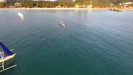 Aerial-shot-of-a-sailboat-passing-through-the-frame-with-the-shoreline-in-front-of-it