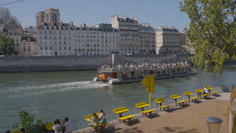 Tourist-Boat-In-Quais-De-Seine-Area-Of-Paris-France-With-People-On-Banks-Of-River-1