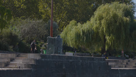 View-From-River-Seine-Of-Tourists-And-Cyclists-On-Quais-de-Jussieu-In-Paris-France