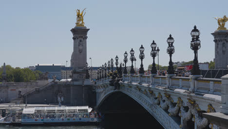 Tourist-Boat-Going-Under-Pont-Alexandre-III-Bridge-Crossing-River-Seine-In-Paris-France-With-Tourists-And-Traffic