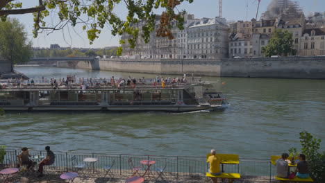 Touristenboot-Im-Viertel-Quais-De-Seine-In-Paris,-Frankreich,-Mit-Menschen-Am-Ufer-Des-Flusses