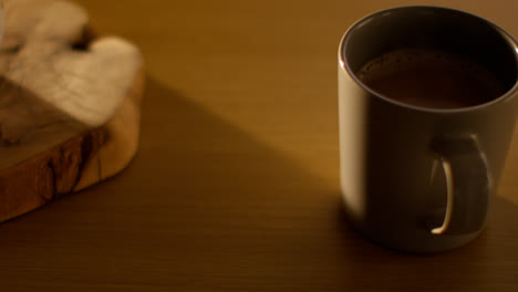 Close-Up-Of-Person-Putting-Down-Steaming-Cup-Of-Hot-Chocolate-Drink-On-Table