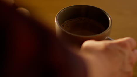 Close-Up-Of-Person-Picking-Up-Steaming-Cup-Of-Hot-Chocolate-Drink-On-Table