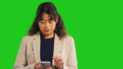 Close-Up-Studio-Shot-Of-Businesswoman-Using-Mobile-Phone-To-Message-Or-Browse-Online-Standing-Against-Green-Screen