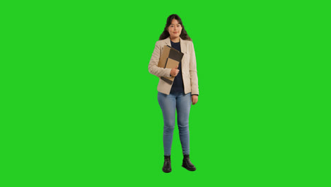 Full-Length-Studio-Portrait-Of-Female-Teacher-Or-Businesswoman-Standing-Against-Green-Screen-Carrying-Folder