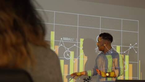 Male-Teacher-Giving-Maths-Or-Science-Lesson-In-College-Or-University-Standing-At-The-Front-Of-Class-With-Projection-Of-Graph-2