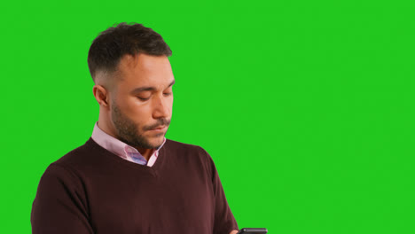 Close-Up-Studio-Shot-Of-Businessman-Using-Mobile-Phone-To-Message-Or-Browse-Online-Standing-Against-Green-Screen-1